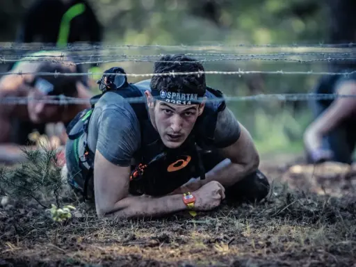 En deltagare i ett ocr sport-lopp kryper under taggtråd.