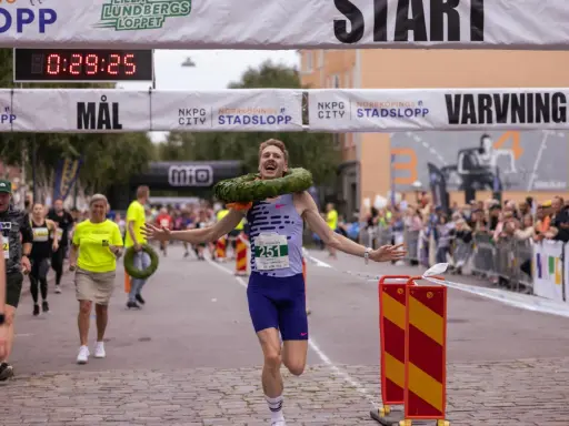 Glad löpare med krans korsar mållinjen i Norrköping stadslopp.