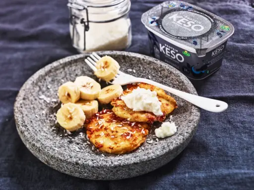 En tallrik med pannkakor toppade med keso och bananskivor. Perfekt för ett proteinrikt keso mellanmål.
