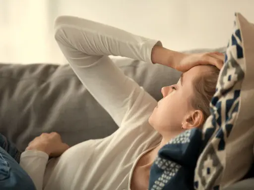 Kvinna med b2 brist ligger på en soffa med handen mot pannan, ser ut att ha ont.