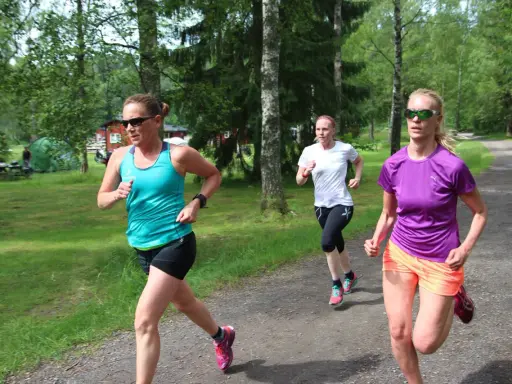 Tre kvinnor springer på en grusväg i en skogsmiljö, zon 2.