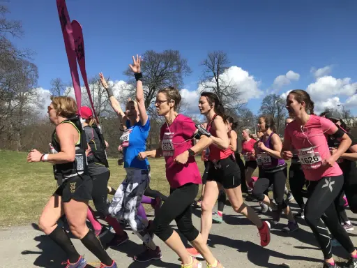 A group of women in running gear race on a sunny day, some with arms raised.