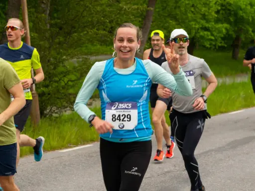 Glada löpare i ett 10 km lopp. En kvinna med nummer 8429 ler och gör segertecken.