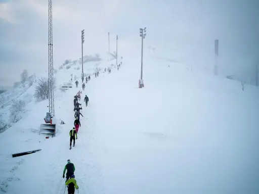 Deltagare i Hammarby Alpin Marathon kämpar sig uppför en snöig backe med skidstavar.