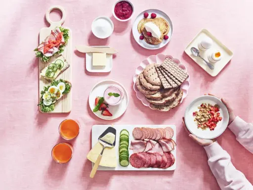 En härlig svensk frukost med smörgåsar, pannkakor, yoghurt, frukt, charkuterier och juice.
