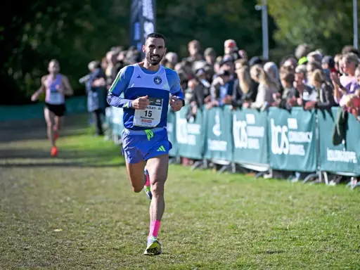 Löpare med nummer 15, klädd i blått och med rosa strumpor, springer mot publiken. En annan löpare syns i bakgrunden. Kanske är det en del av sevilla marathon.