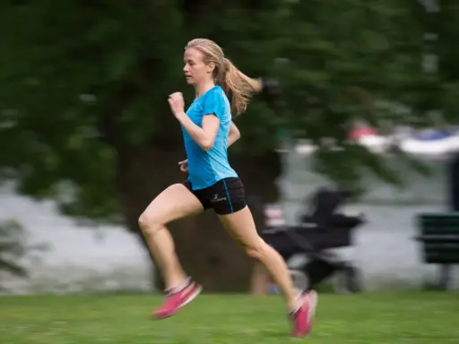 En person som springer snabbt över en grön gräsmatta, med träd och en sjö i bakgrunden.