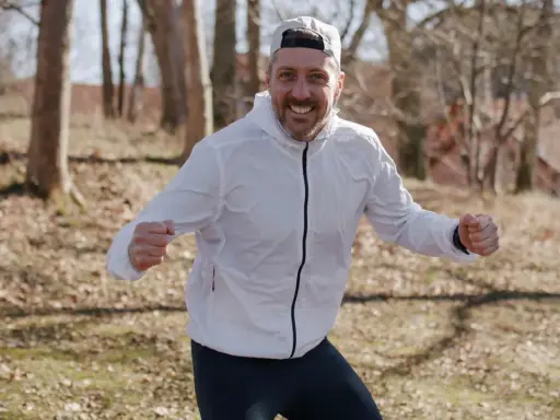 Glad löpare i vit jacka och keps, redo att springa. Undrar hur lång tid det tar att springa 1 mil?