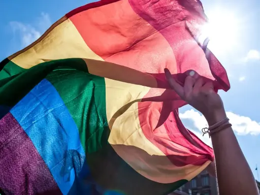 En hand håller en regnbågsflagga mot en solig himmel. En symbol för att **run for pride** och kärlek.