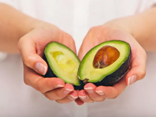 Händerna håller en avokado, delad på mitten, som visar dess gröna kött och bruna kärna. En näringsrik källa till avokado vitaminer.