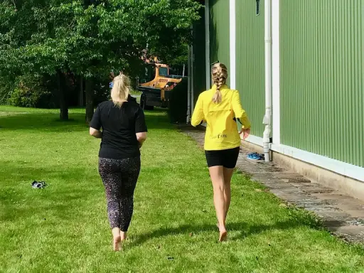 Två kvinnor njuter av en löprunda barfota på gräset en solig dag.