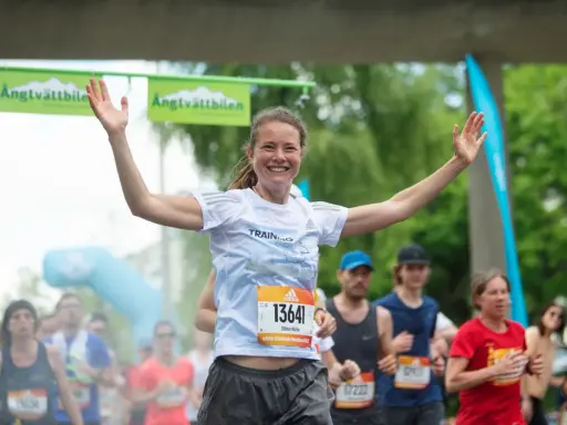 Glad kvinna med armarna uppe vid målgången i ett maraton. En lycklig löpare som njuter av sin maraton tid.