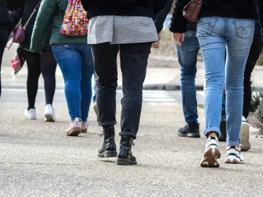En grupp människor går på en trottoar. De har på sig jeans och sneakers. Kanske är de på väg att nå sina 10000 steg kcal.