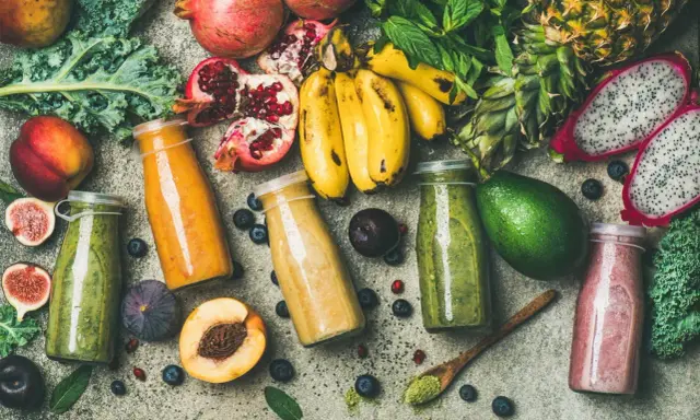 Färgglada smoothies i flaskor, omgivna av färsk frukt och grönsaker. En visuell påminnelse om vad betyder detox för kroppen.