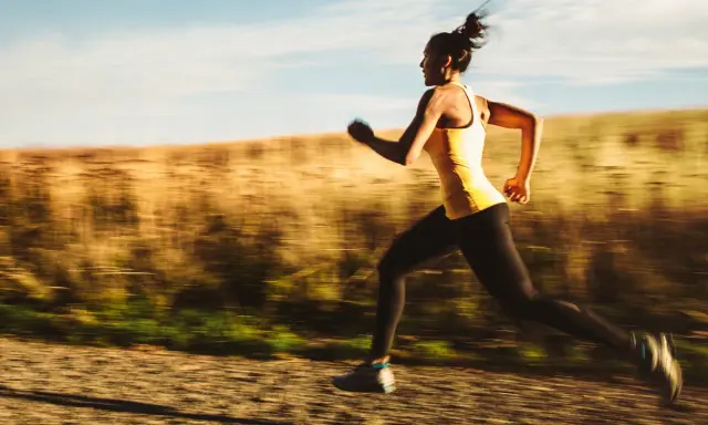 Kvinna i gult linne och svarta tights springer snabbt på en grusväg, en del av ett intensivt hiit pass.