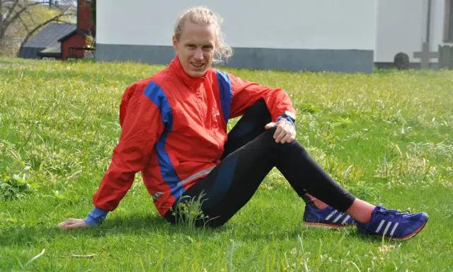 En löpare i röd jacka och svarta tights vilar i gräset, redo att springa milen under 50 minuter.