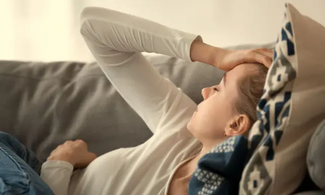 Kvinna med b2 brist ligger på en soffa med handen mot pannan, ser ut att ha ont.