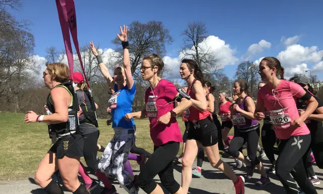 A group of women in running gear race on a sunny day, some with arms raised.