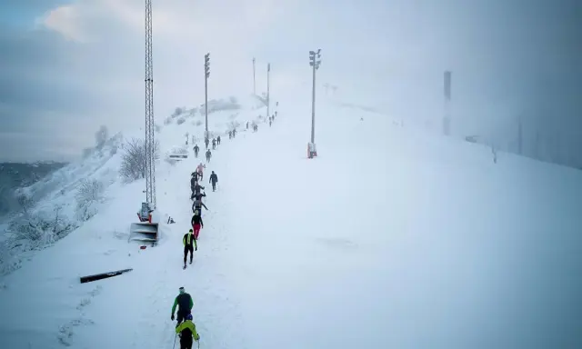 Deltagare i Hammarby Alpin Marathon kämpar sig uppför en snöig backe med skidstavar.