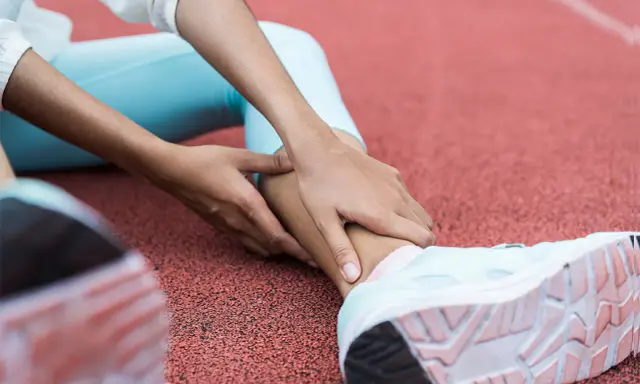 Person på löparbana med händer på underbenet, troligen för rehab benhinneinflammation.