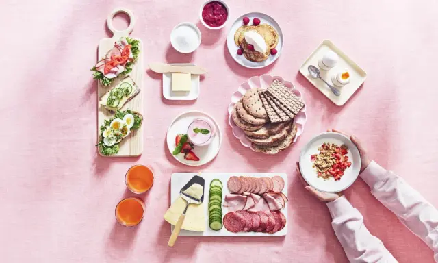 En härlig svensk frukost med smörgåsar, pannkakor, yoghurt, frukt, charkuterier och juice.