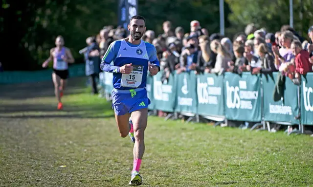 Löpare med nummer 15, klädd i blått och med rosa strumpor, springer mot publiken. En annan löpare syns i bakgrunden. Kanske är det en del av sevilla marathon.