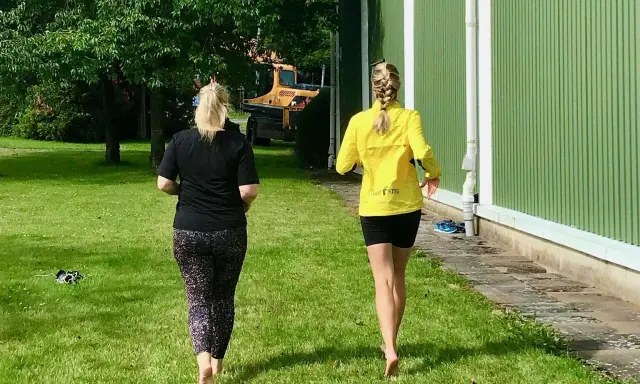 Två kvinnor njuter av en löprunda barfota på gräset en solig dag.