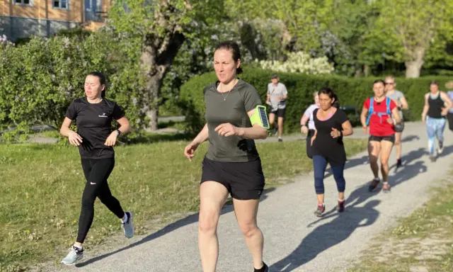 En grupp löpare på en grusväg, kanske på väg att klara 1 mil. Solen skiner och träden är gröna.