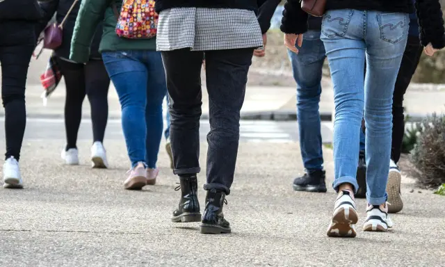 En grupp människor går på en trottoar. De har på sig jeans och sneakers. Kanske är de på väg att nå sina 10000 steg kcal.