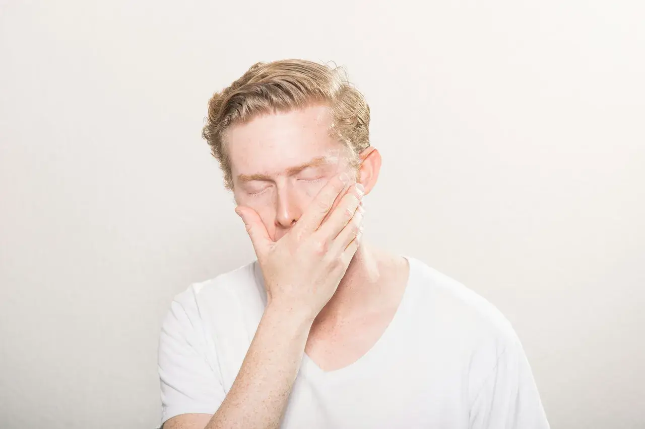 Man med slutna ögon och hand över munnen, som om han drabbats av en plötslig kramp i tårna brist.