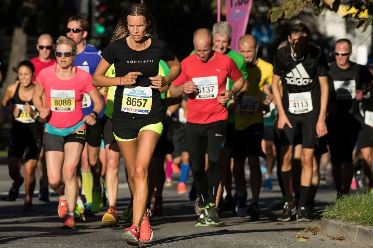 Löpare i Stockholm Halvmarathon, fokus på nummer 8657. En kvinna i förgrunden med nummerlapp, tävlar mot klockan för bästa halvmaraton tid.