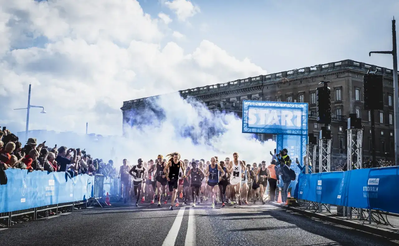 L&ouml;pare startar adidas halvmarathon i Stockholm, omgivna av publik och bl&aring; r&ouml;k.
