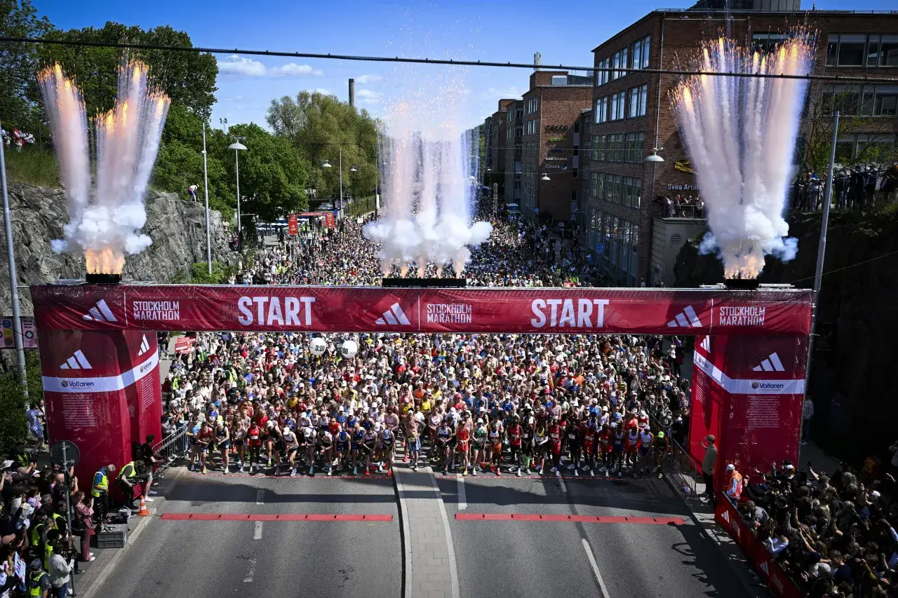 Startskottet för rekord Stockholm Marathon avfyras med fyrverkerier. Tusentals löpare redo vid startlinjen.