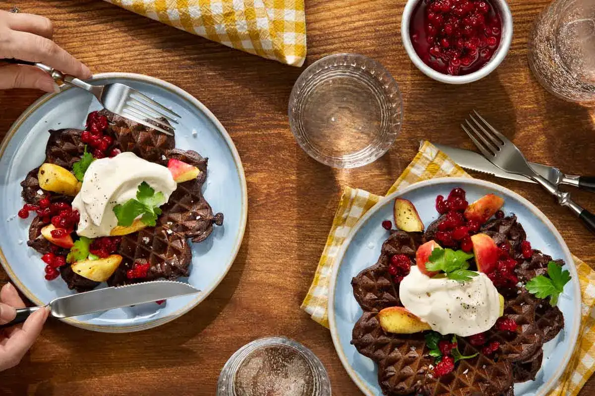 Tv&aring; tallrikar med chokladv&aring;fflor, toppade med gr&auml;dde, lingon och &auml;ppelbitar. En h&auml;rlig svensk frukost som ser uts&ouml;kt ut.