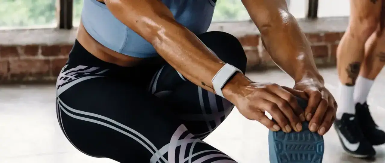 Svettig person str&auml;cker sig, b&auml;r tr&auml;ningskl&auml;der och ett armband som visar HRV status.
