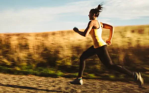 Kvinna i gult linne och svarta tights springer snabbt på en grusväg, en del av ett intensivt hiit pass.