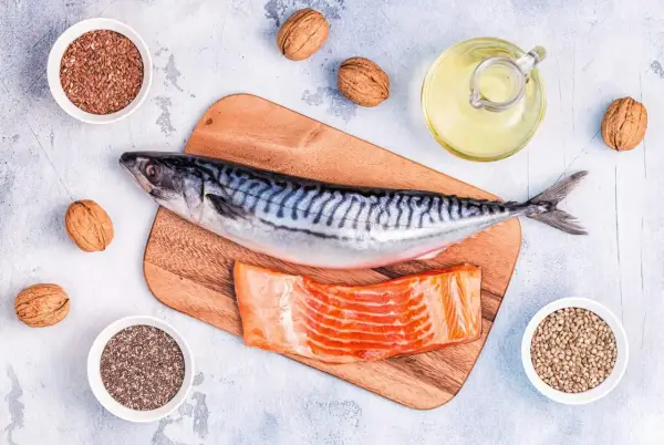 Makrill, laxfilé, valnötter och frön som linfrön, chiafrön och hampafrön. En flaska med olja, kanske rapsolja omega 3, står bredvid.