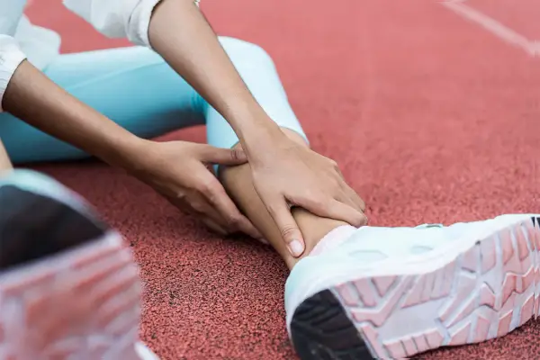 Person på löparbana med händer på underbenet, troligen för rehab benhinneinflammation.