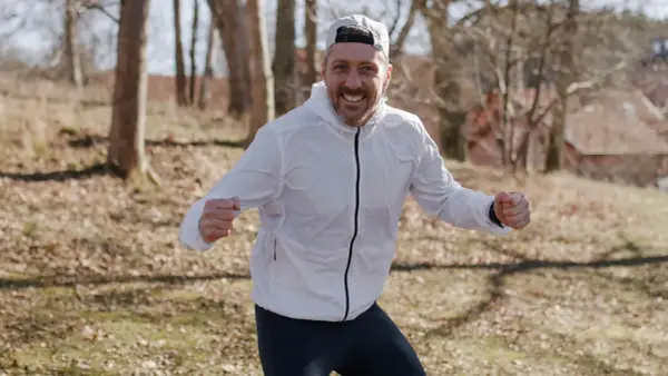 Glad löpare i vit jacka och keps, redo att springa. Undrar hur lång tid det tar att springa 1 mil?