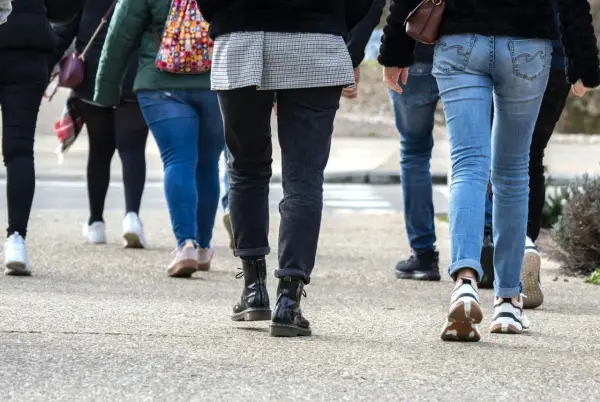 En grupp människor går på en trottoar. De har på sig jeans och sneakers. Kanske är de på väg att nå sina 10000 steg kcal.