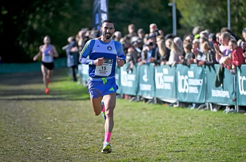 Löpare med nummer 15, klädd i blått och med rosa strumpor, springer mot publiken. En annan löpare syns i bakgrunden. Kanske är det en del av sevilla marathon.